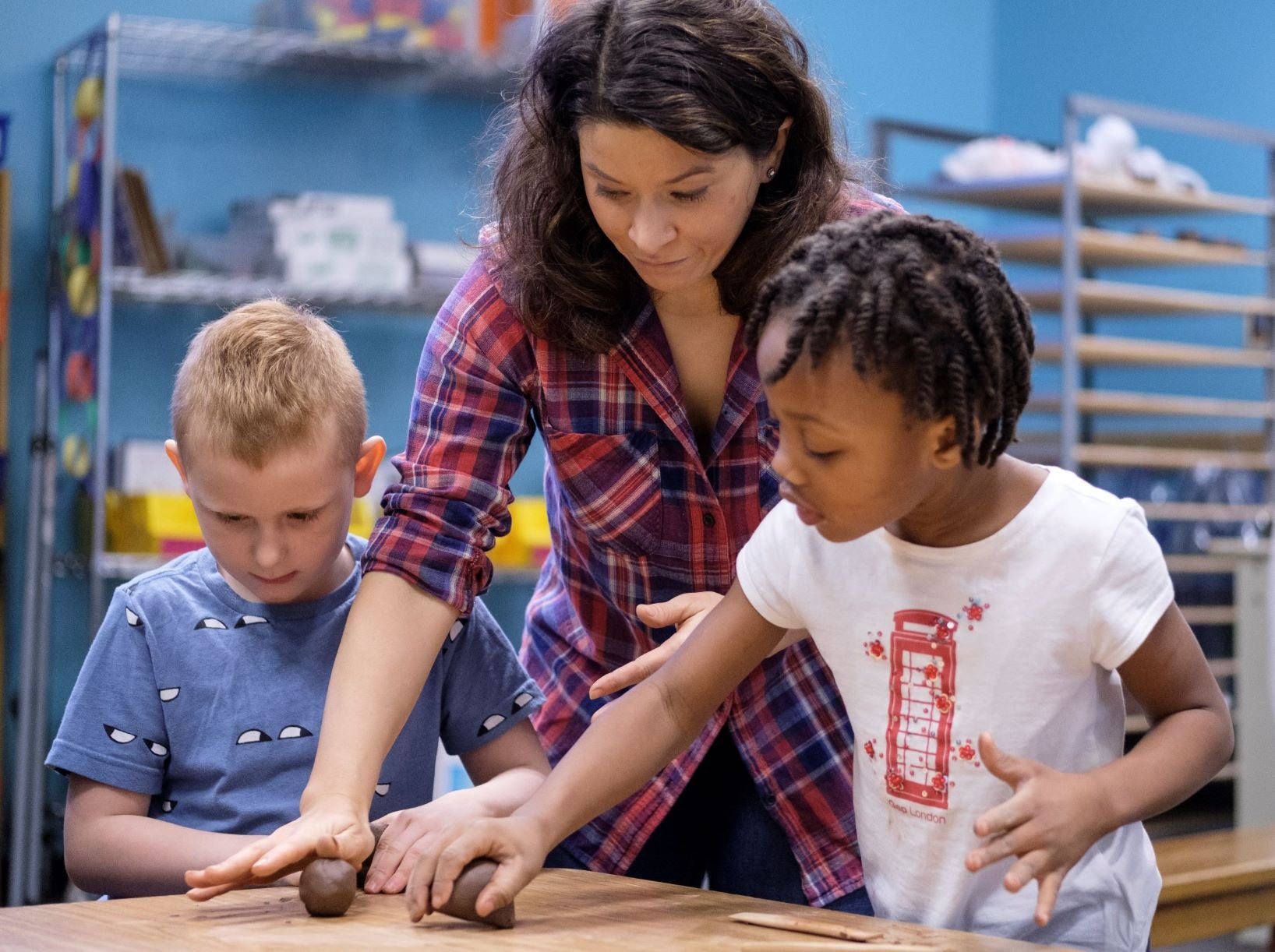 teacher working with two elementary students on a clay project