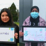 A group of students pose with a hand drawn sign that says welcome in different languages