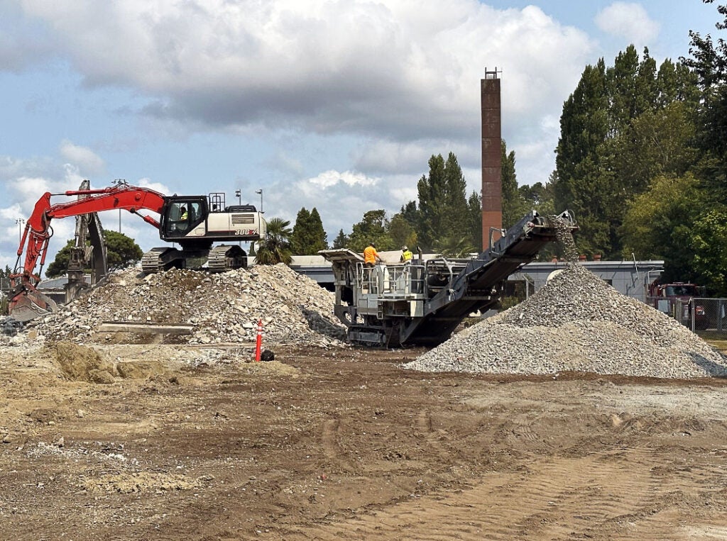 an expanse of concrete leads to two partially demolished buildings - one on each side - each has an excavator doing demolition