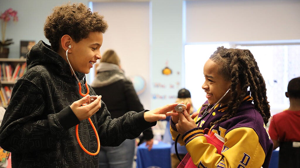 Students wear stethoscopes and practice using them together in a classroom