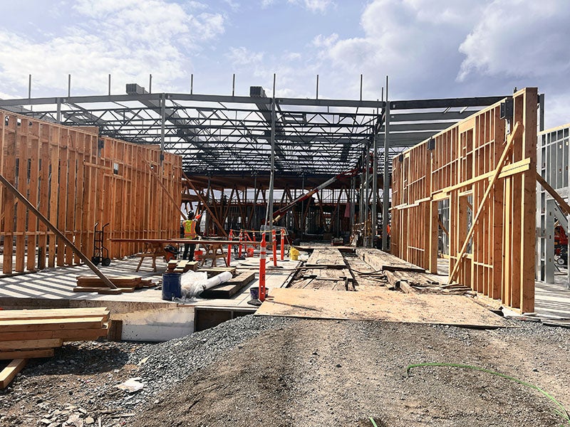 a building under construction with steel truss being installed for the roof and some wood wall framing in place