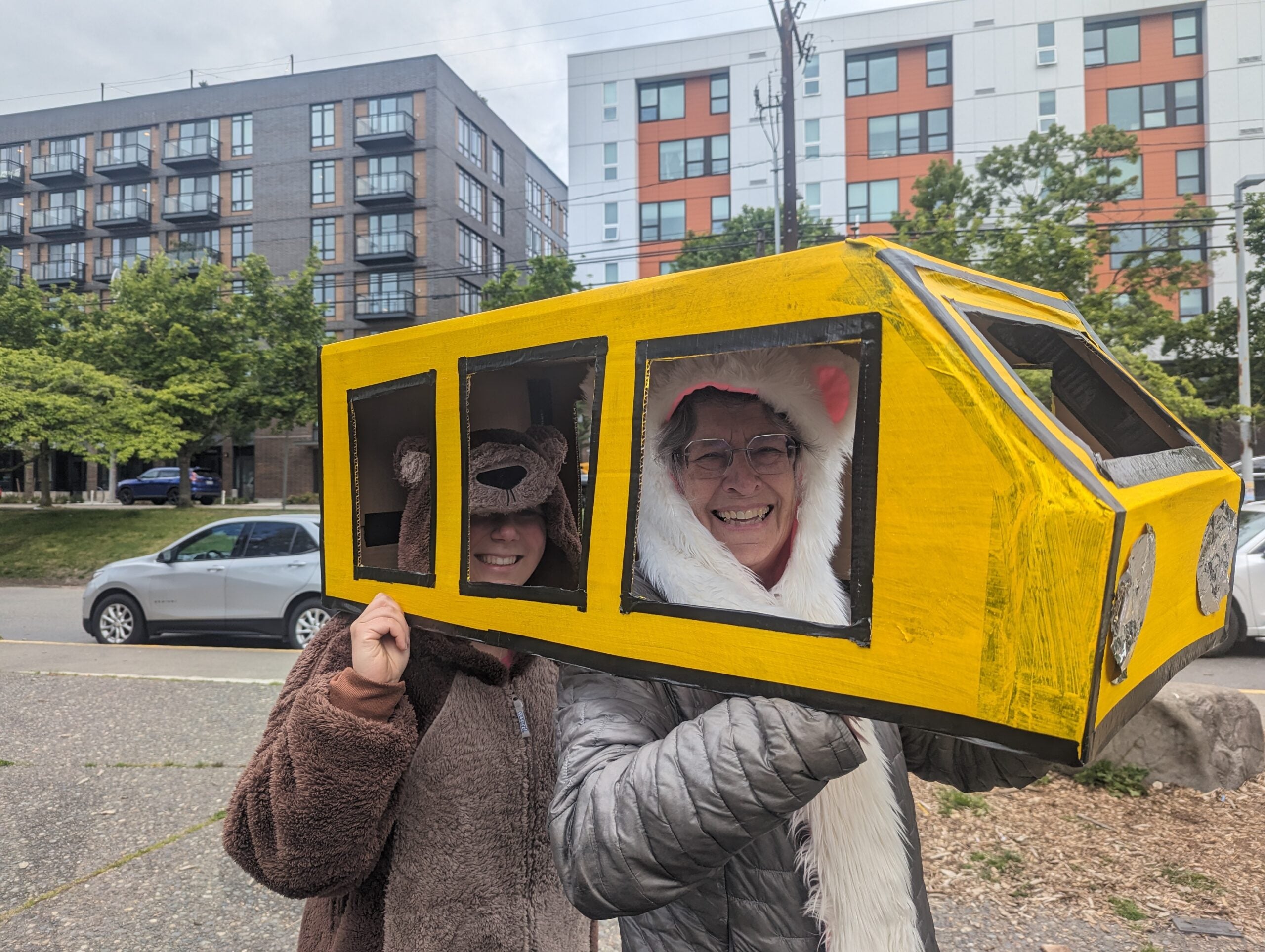 two adult volunteers in bear costumes pose inside cardboard "walking school bus" outside of Bailey Gatzert
