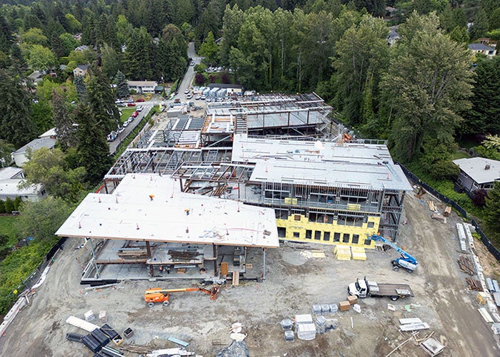 aerial view of a large building under construction with roofs in place in two areas and framing on others