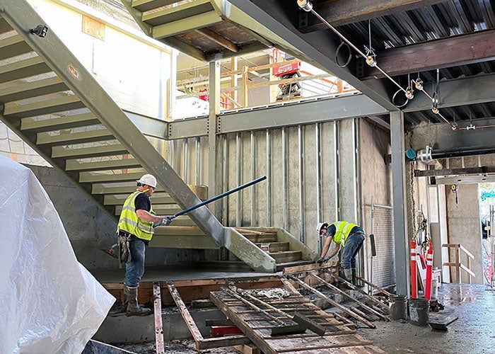 interior of a partially built wall and ceiling with a stairway being built by 2 workers