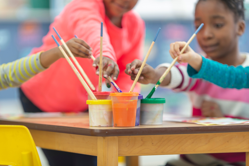 elementary students dipping paintbrushes into paint