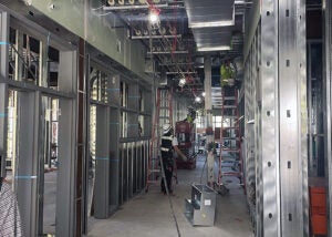 inside a partially constructed hallway with metal studs and people working