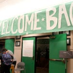 Three students gather at a table under a sign that says Welcome Back