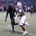 Two high school football players in uniform and helmets practice on a field