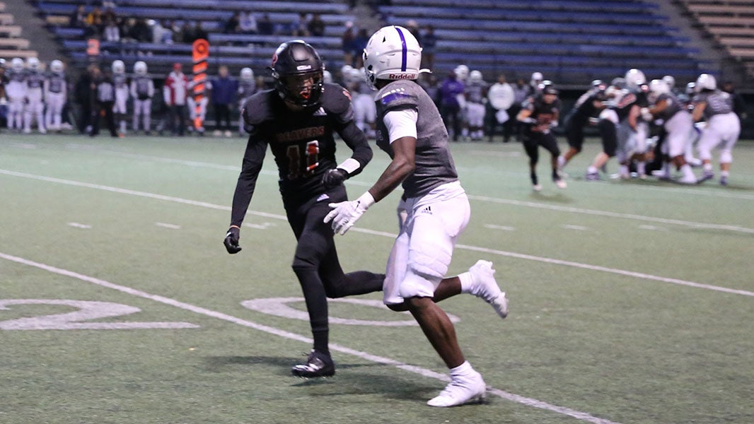 Two high school football players in uniform and helmets practice on a field