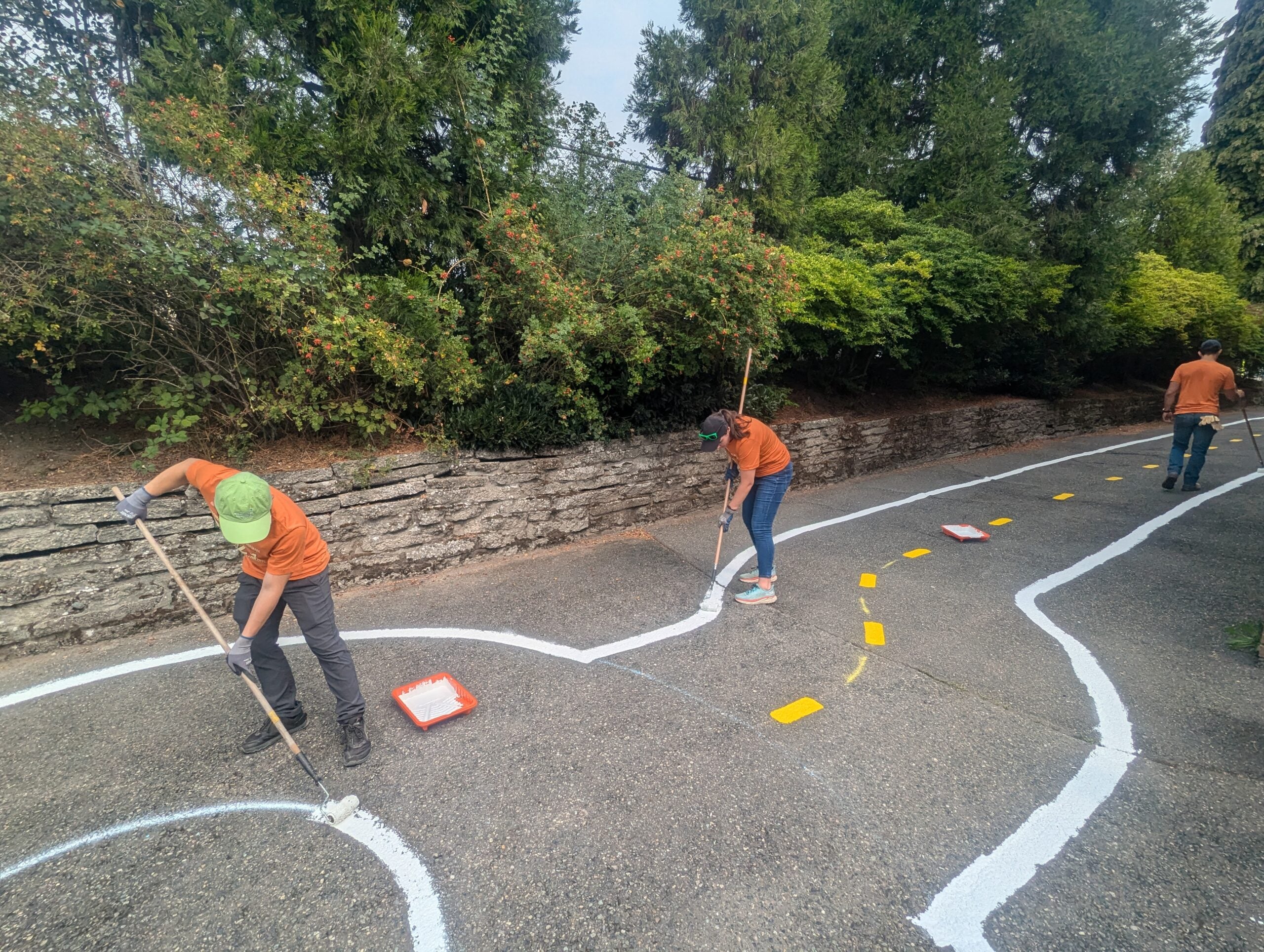 Three volunteers paint traffic garden street lines on pavement.