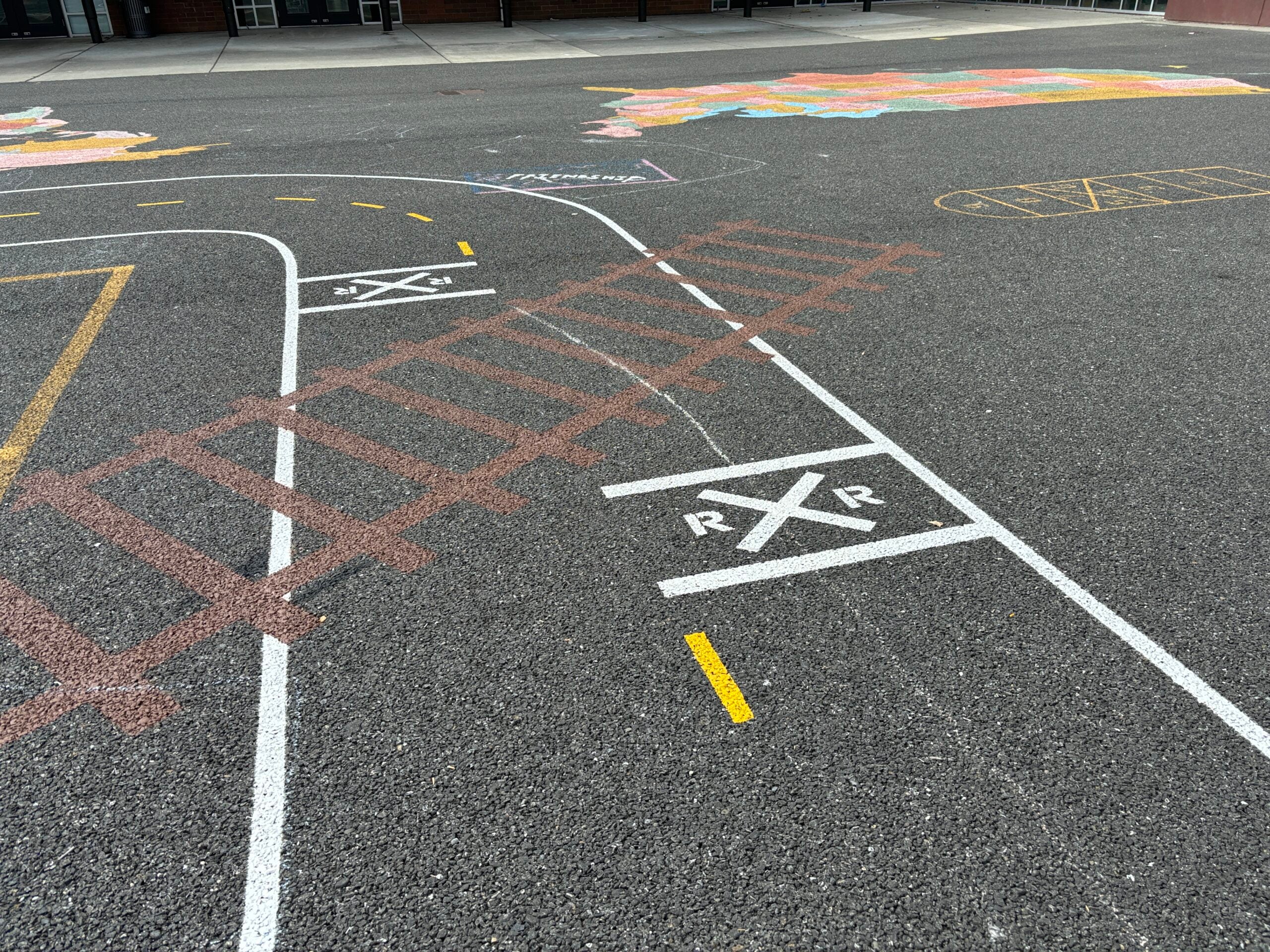 Miniature road painted on blacktop with painted railroad tracks.