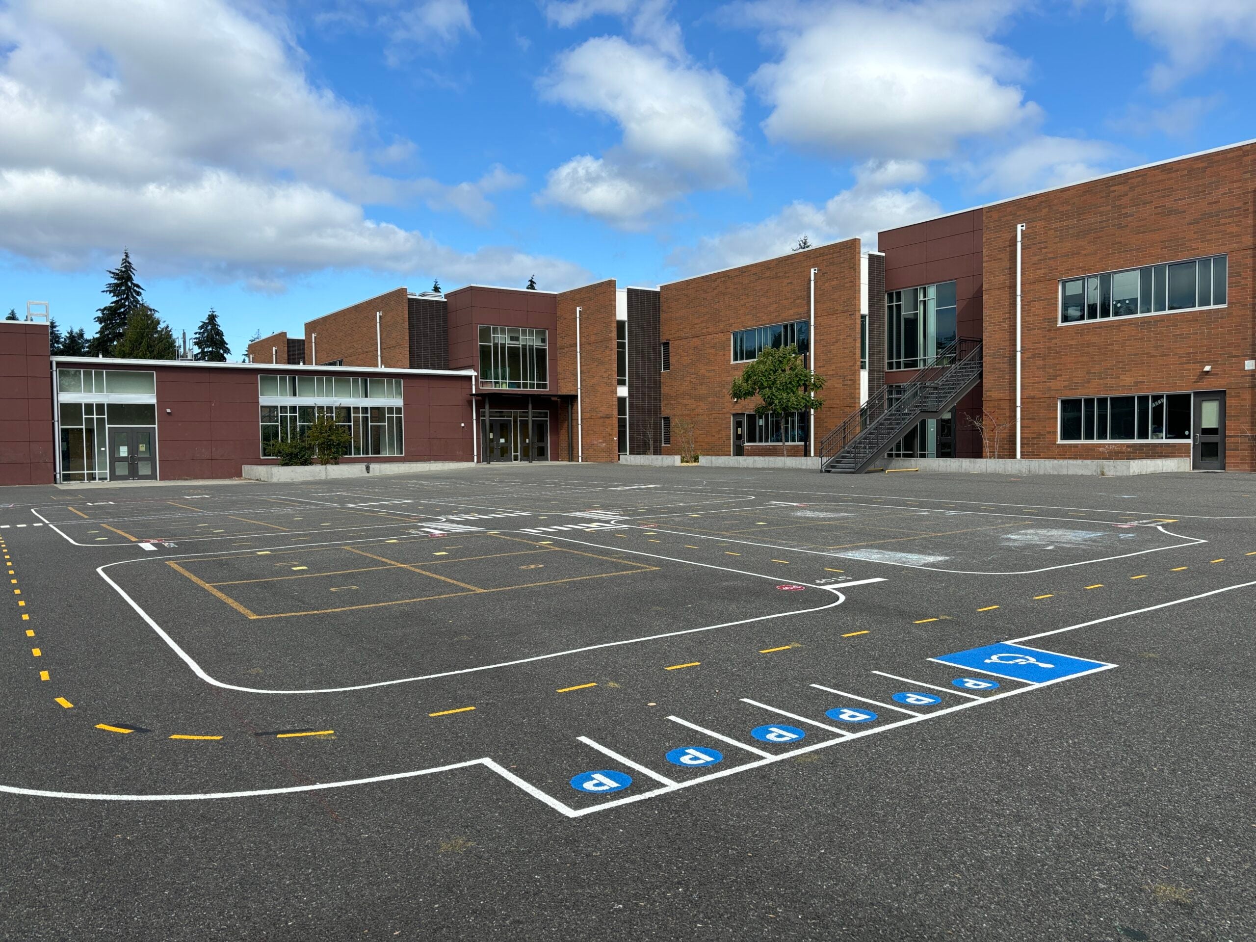 Miniature road with parking stalls painted on blacktop with school in background.