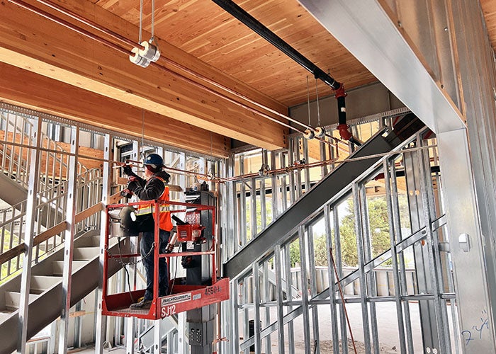 a person is on a lift working on copper pipes near the wooden ceiling and beams