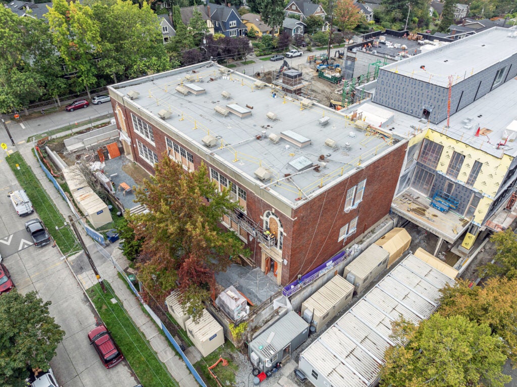 brick building with trees in front and a building under construction attached