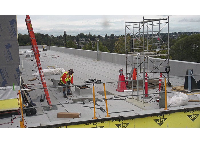 part of a flat roof with a ladder and scaffold and a worker in a vest and hardhat