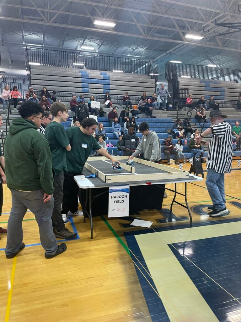 Image of high school students wearing green shirts competing in a robotics compeition