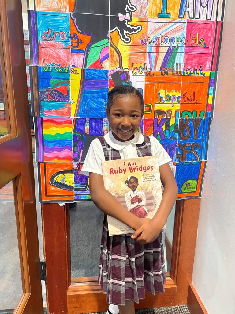 Student dressed as Ruby Bridges poses in front of ruby bridges student art wall.