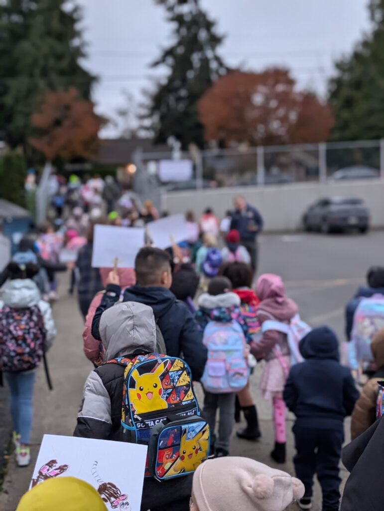 Students hold signs and walk in group to school entrance.