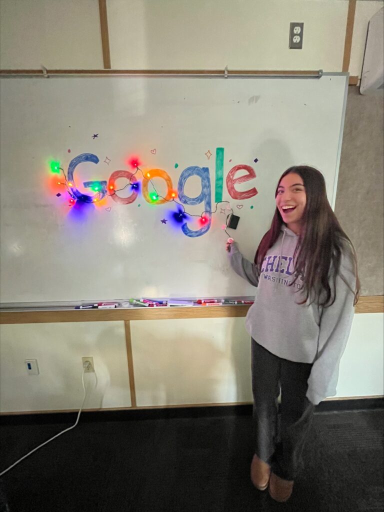 Studnet poses next to whiteboard welcoming Google volunteers