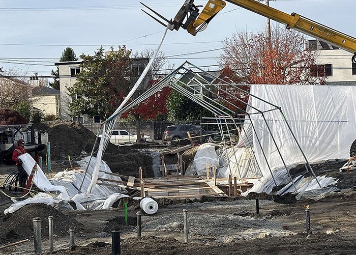 a metal tent frame with a machine lifting canvas up over it