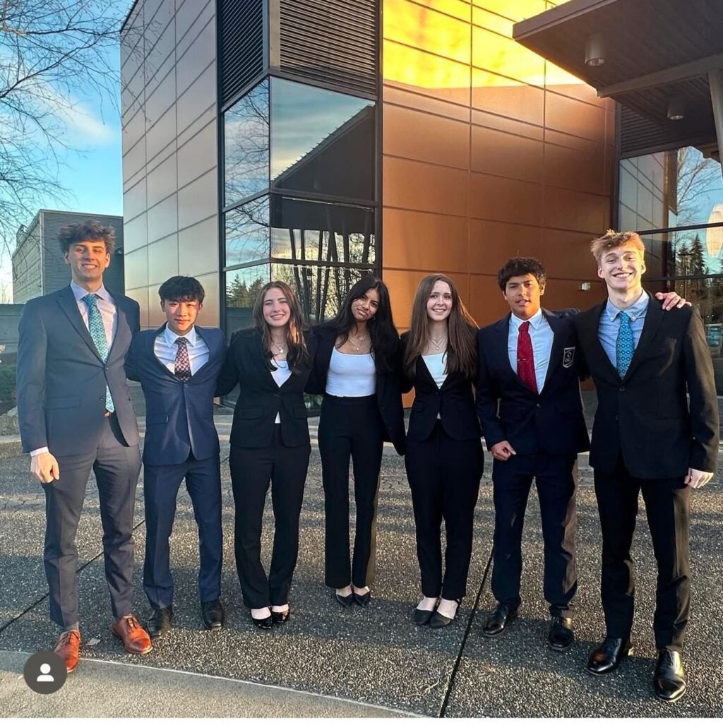 Group of students wearing suits in front of modern building