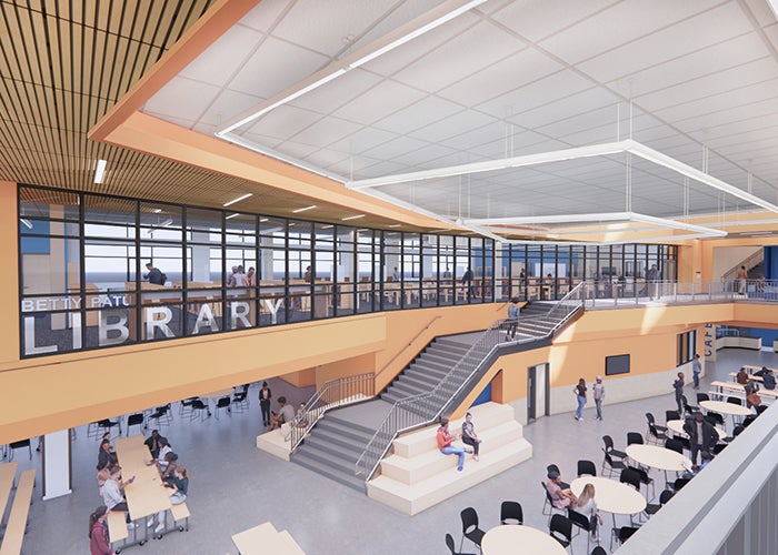 large common area with dining tables and stairs; a room with glass windows looking out toward below says LIBRARY