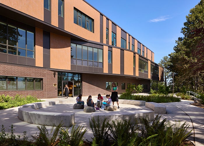 a concrete block seating circle outside of a 3 store brown building with a wavy wall