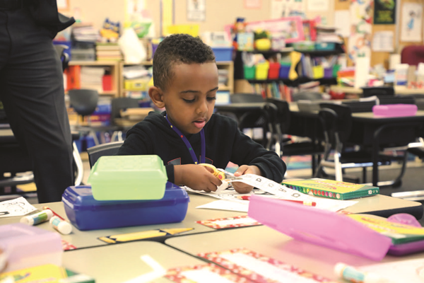 Preschool student cutting a piece of paper with scissors