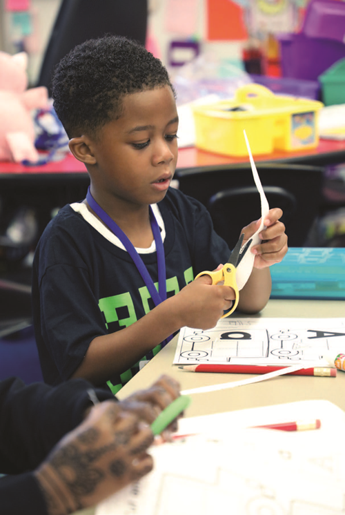 Preschool student cutting a piece of paper with scissors