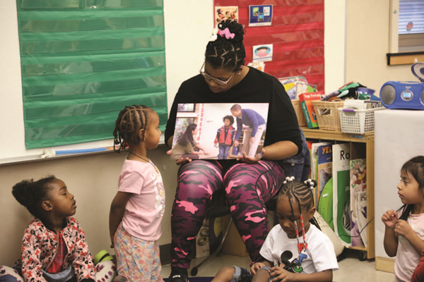 Preschool teacher readnig a book to students