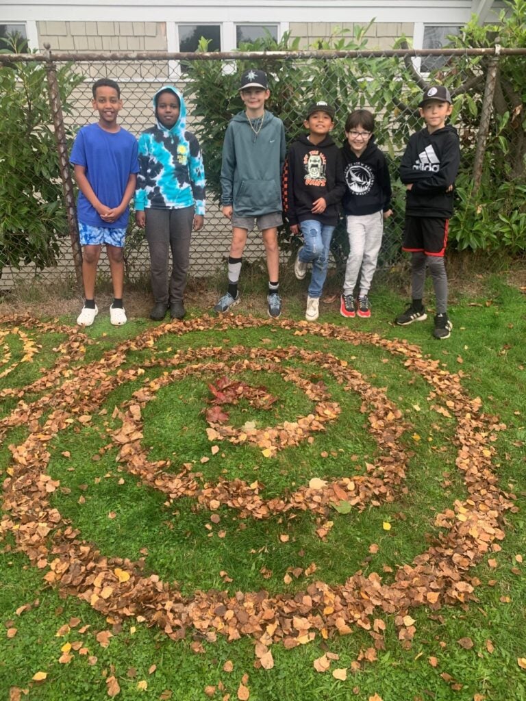 students standing in front of fence and their art installation made with leaves